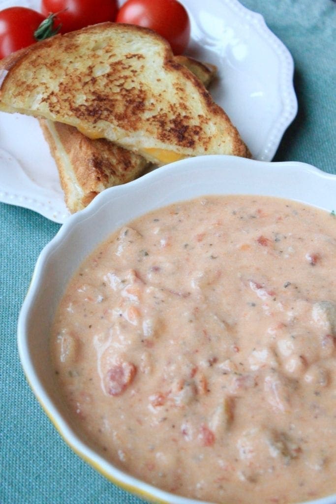 Creamy Tomato Basil Soup Creamy Tomato Basil Soup in a bowl with a grill cheese sandwich in the background on a white plate with tomatoes