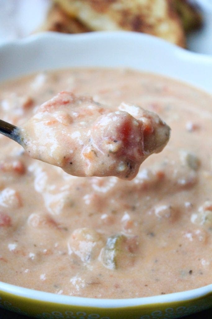 Spoon full of Creamy Tomato Basil Soup hovering over a bowl with a blurry grill cheese sandwich in the background