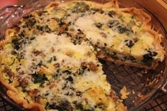 Sausage Spinach Quiche in a glass pie pan with one slice out of it