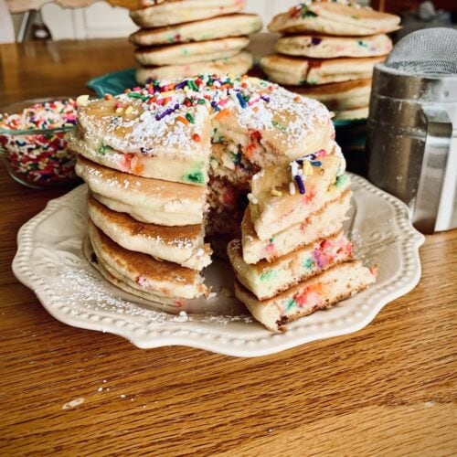 Three massive stacks of cake Batter pancakes with sprinkles and powdered sugar