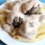 Swedish Meatballs covered in sauce over noodles sitting on a round plate and wood table