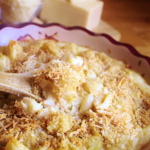 Wooden spoon holding a helping of White cheddar and parmesan Macaroni and cheese above a pie plate