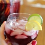 Hand holding glass full of Sparkling Summer Sangria in front a a picture of the beverage