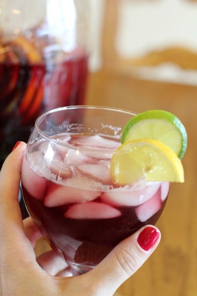 Hand holding glass full of Sparkling Summer Sangria in front a a picture of the beverage