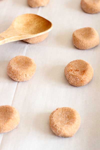 balls of cream cheese snickerdoodle dough being swashed with wooden spoon on parchment paper