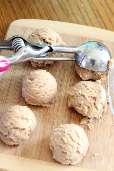 Silver scoop placing six balls of cream cheese snicker doodle dough on a wood cutting table.