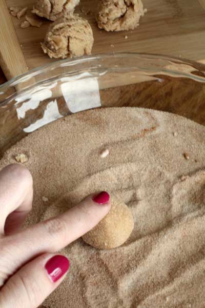 ball of cream cheese snickerdoodle dough being rolled in sugar