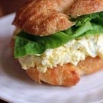 Deluxe Egg Salad sandwich on a white plate and wood table.