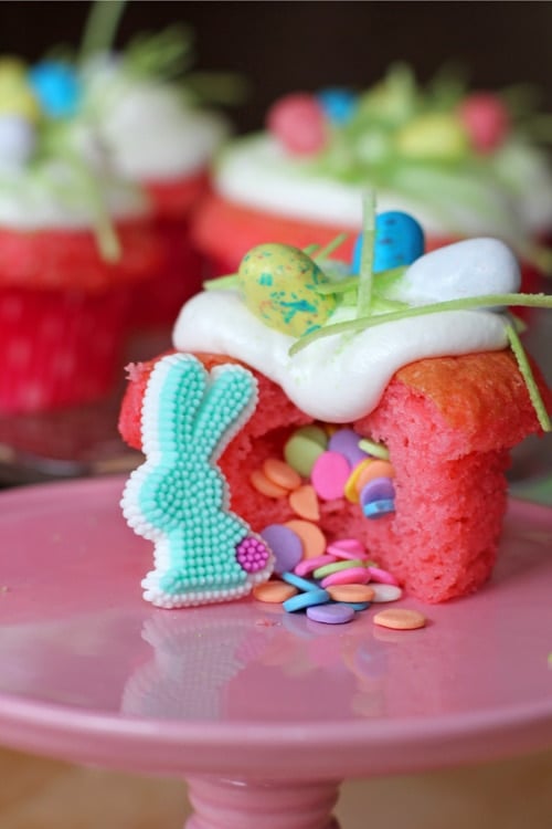 Easter Surprise Cupcakes sitting on a pink cake tray with colorful background