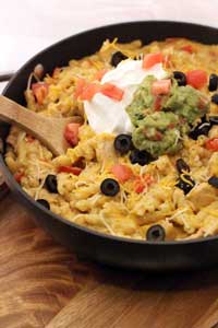 Chicken Enchilada Pasta with sour cream and guacamole in a pan with wooden spoon