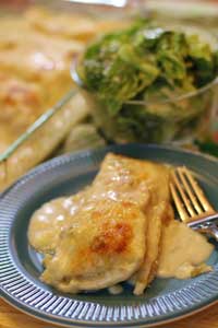 White Chicken Enchilada On a round plate with fork and bowl of salad in the background