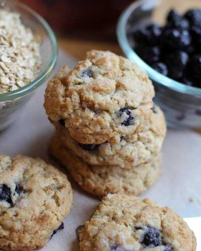 Blueberry cookies stacked next to bowls of blueberries