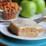 White plate with Carmel Apple cake and blurry apples in the background