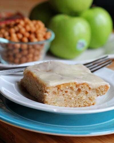 White plate with Carmel Apple cake and blurry apples in the background