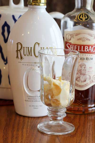 clear glass with hot butter batter inside, sitting on a wood table in front of two bottles of rum