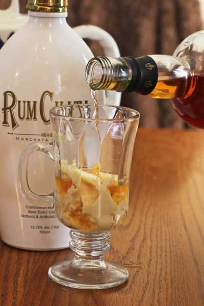 Rum being poured into a clear glass sitting on a wood table