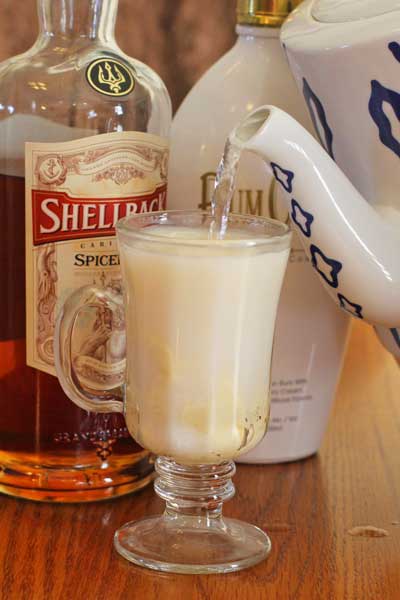 Hot water being added to the Hot Buttered Rum beverage in a clear glass sitting on a table