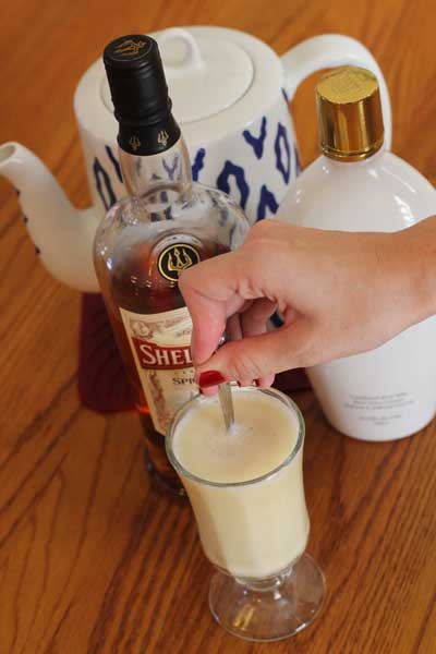 Hand stirring hot buttered rum in a clear glass  in front of three bottles of rum