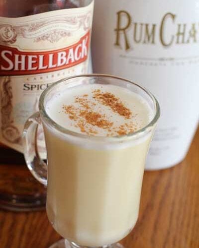 Hot Buttered Rum in a clear glass sitting in fron a a bottle of Spiced rum and Rum Chata