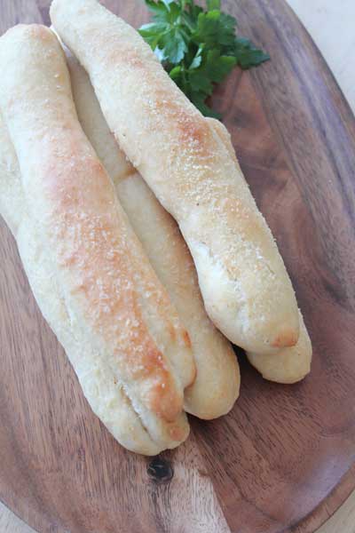 Five home made breadsticks sitting on a wooden tray