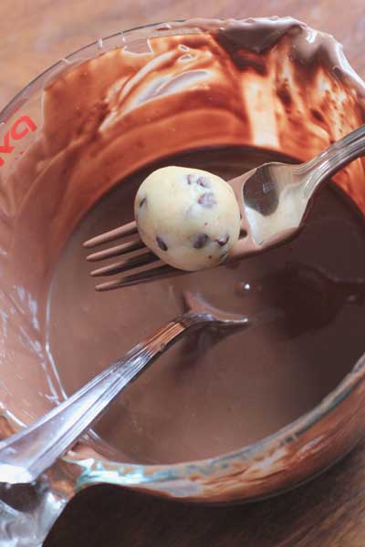 No Bake Cookie Dough Truffles on a fork above a bowl of melted chocolate about to get dunked