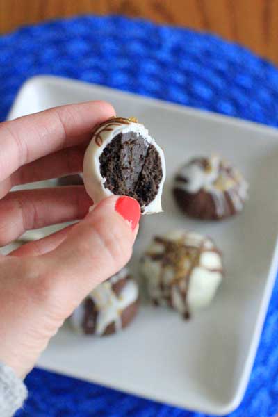 Hand holding a bitten Oreo Truffle above a plate with more chocolate balls on a square plate