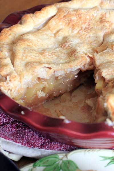 Pie plate with Perfect Apple Pie missing one slice sitting on a wood table