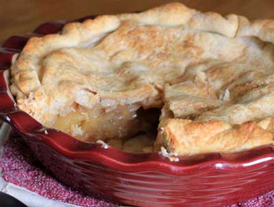 Pie plate with Perfect Apple Pie missing one slice sitting on a wood table