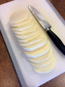 mozzarella cheese sliced on a cutting board next to a knife