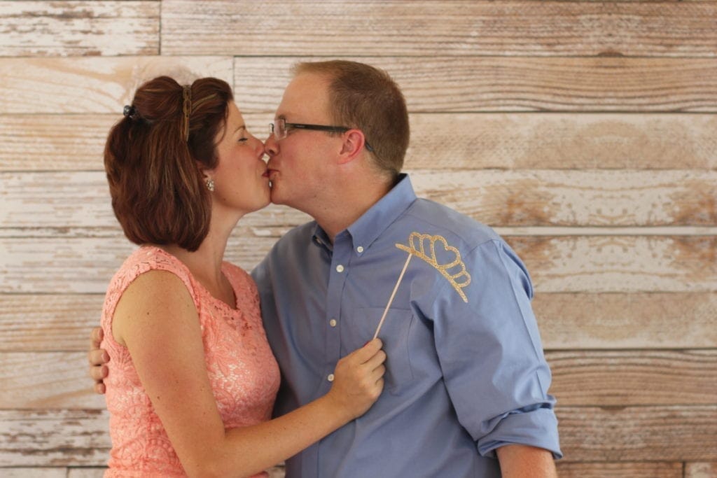 Clint and Lexi kissing in front of a wood background at a party