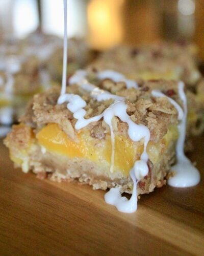 White frosting being drizzled on Peach Crisp Bars sitting on a wood tray