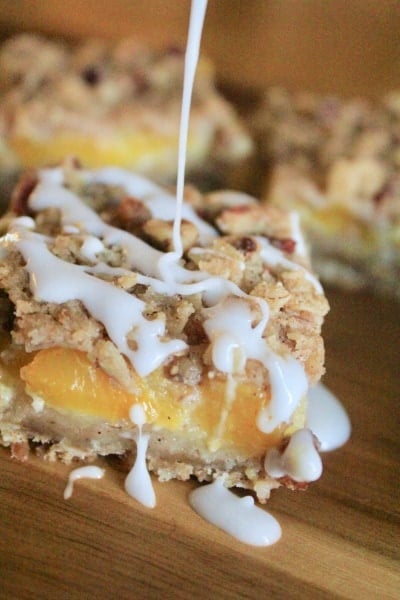 White frosting being drizzled on Peach Crisp Bars sitting on a wood tray