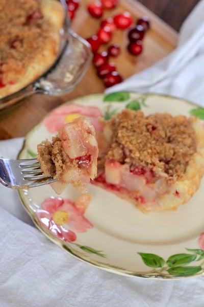 Cranberry Pear Crumb Pie on desert rose plate with cranberries in the background and a fork serving up a delicious bite