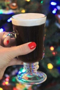 Authentic Irish Coffee in clear glass held up in front of a christmas tree background