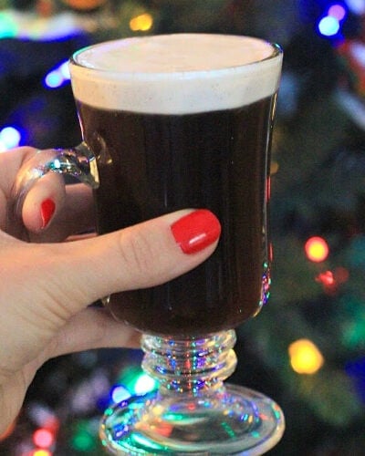 Authentic Irish Coffee in clear glass held up in front of a christmas tree background