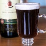 Authentic Irish Coffee in clear glass set on wood table with Irish Whiskey in the background