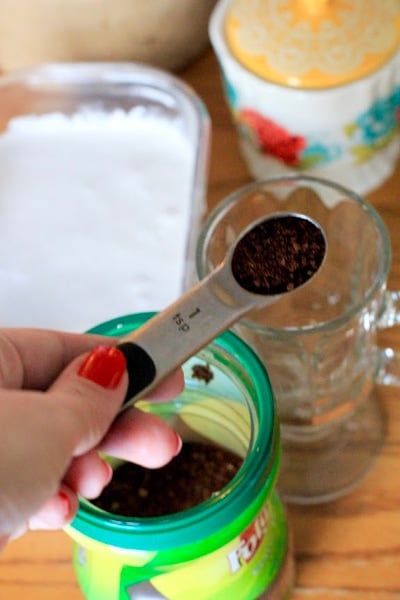 Hand measuring on teaspoon of coffee into a glass mug