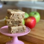 Maple Apple Cake Bars text overlay with image of three cake bars stacked on a pie plate in front of apples on a wood table