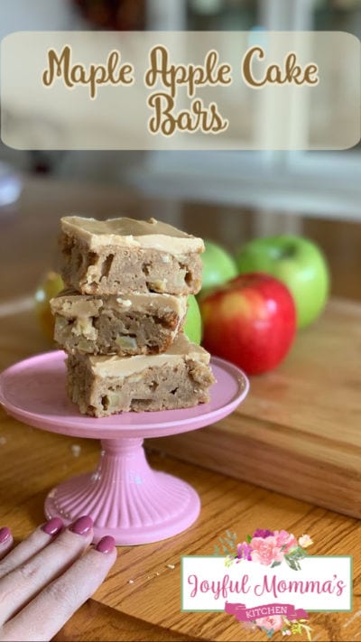 Maple Apple Cake Bars text overlay with image of three cake bars stacked on a pie plate in front of apples on a wood table