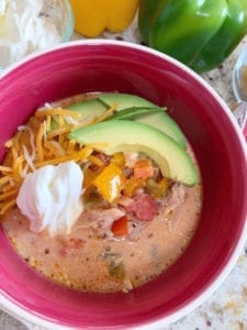 Close up shot of Creamy Chicken Fajita Soup in a bowl next to ingredients on a marble countertop