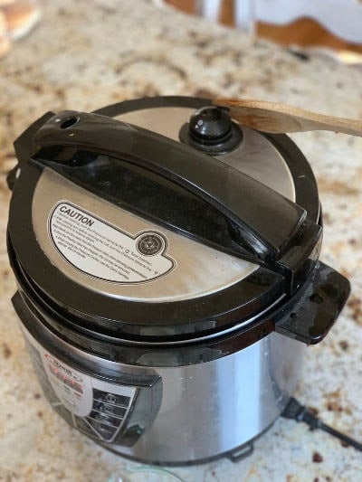 A wooden spoon adjusting the vent of a pressure cooker 