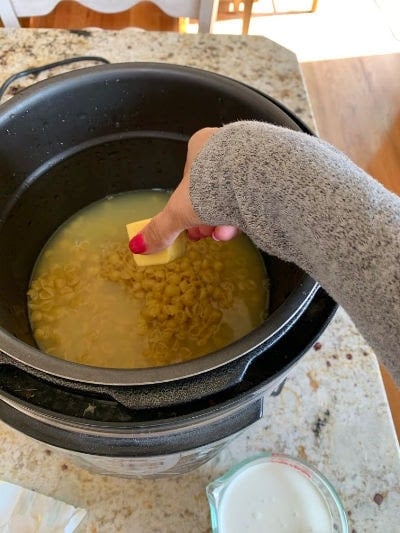 Butter being placed in a pressure cooker on top of noodles and broth