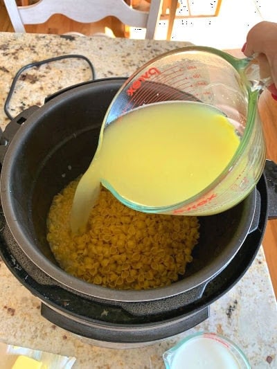 Four cups of broth being poured on the noodles sitting in the pressure cooker