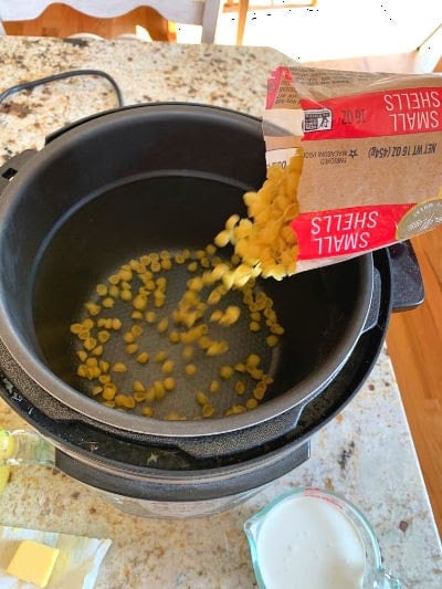 Small shell noodles being poured into a pressure cooker