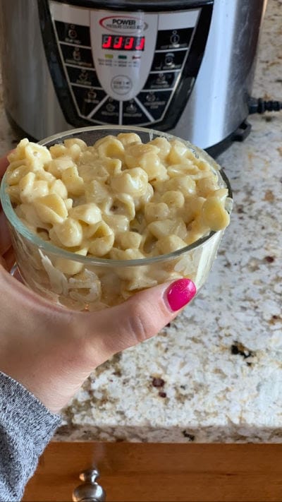 hand holding glass bowl of Instant Pot Mac and Cheese in front of a pressure cooker
