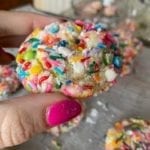 Cookie with sprinkles held by a hand with pink nail polish