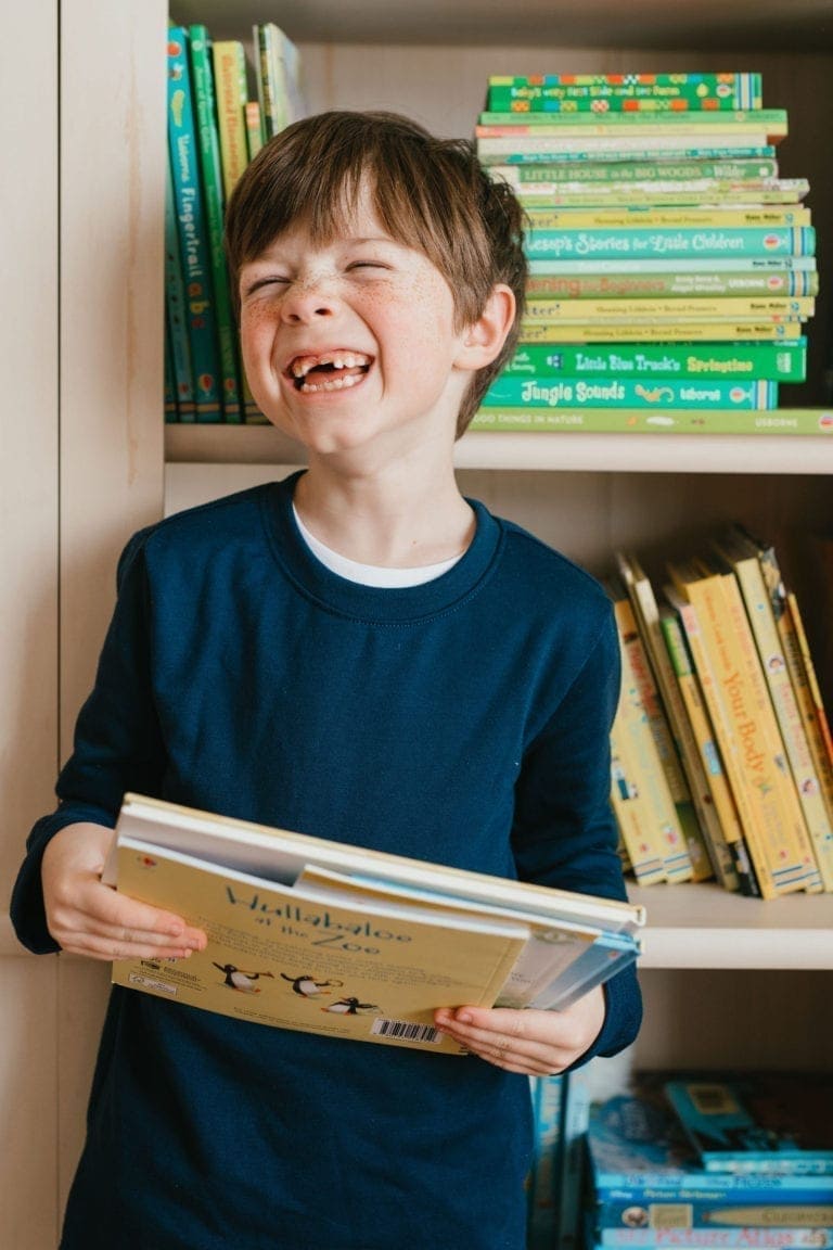 boy missing front teeth laughing while holding books in front of bookshelf