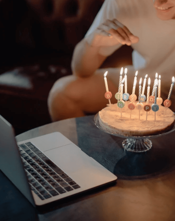 Birthday cake with lit candles held in front of a laptop