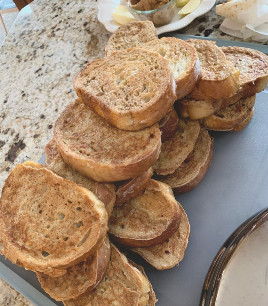 Golden brown French toast stacked high on a cutting board over a marble counter top