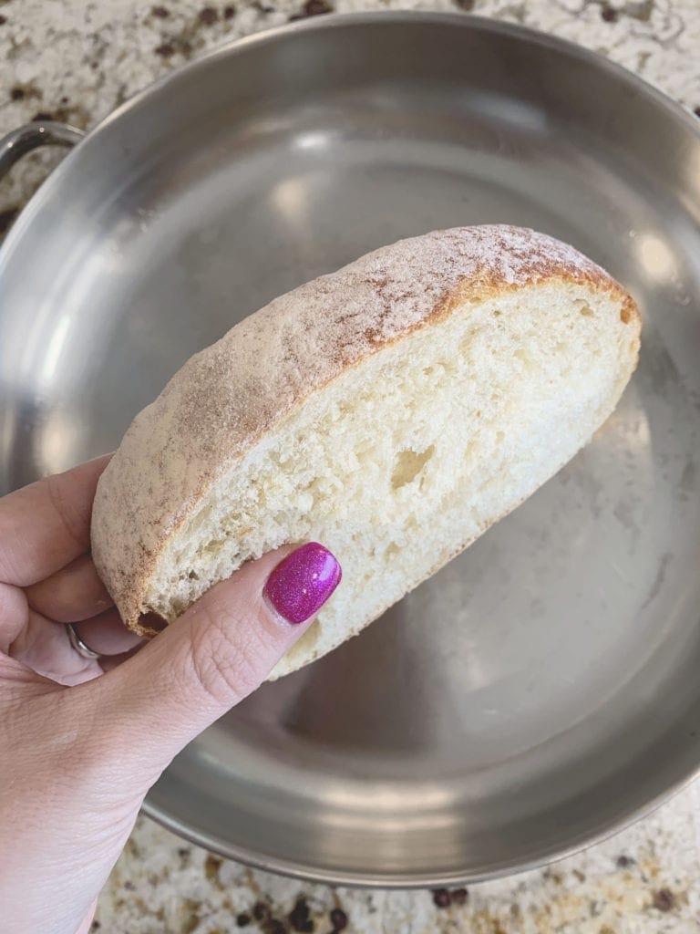 hand with purple nail polish holding Sliced bread above a stainless steel griddle.